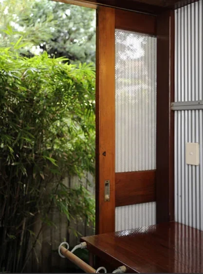 Partially open wooden and metal screen door leading outside with greenery and trees visible.