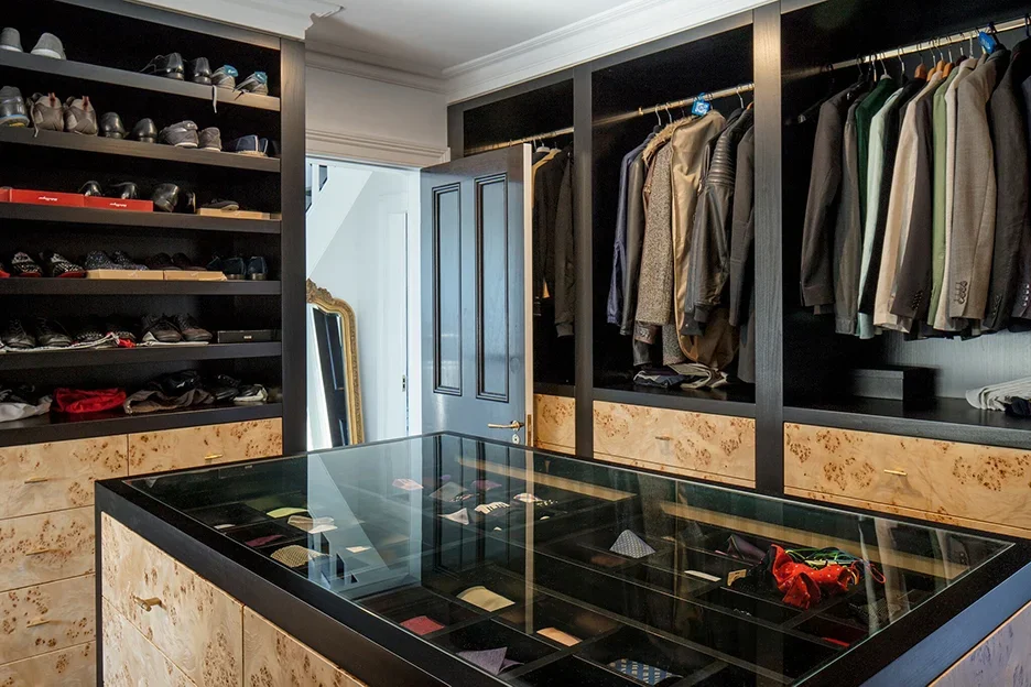 Walk-in closet with shelves of shoes, hanging clothes, and a glass display case in the center.