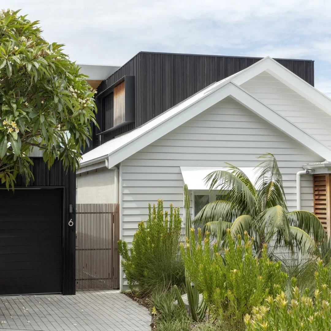 Modern residential house with white and black exterior, featuring a sloped roof, surrounded by green plants and shrubs.