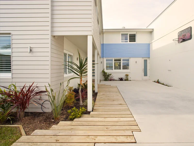 Modern residential outdoor patio with wooden walkway, tropical plants, and basketball hoop