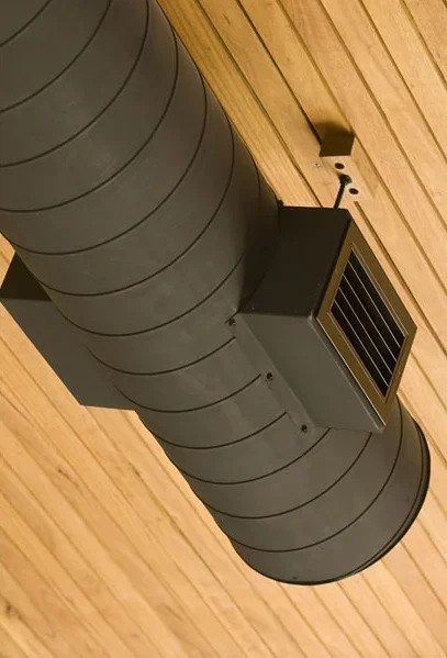 A large gray air ventilation duct with a square vent at the ceiling of a wooden room.