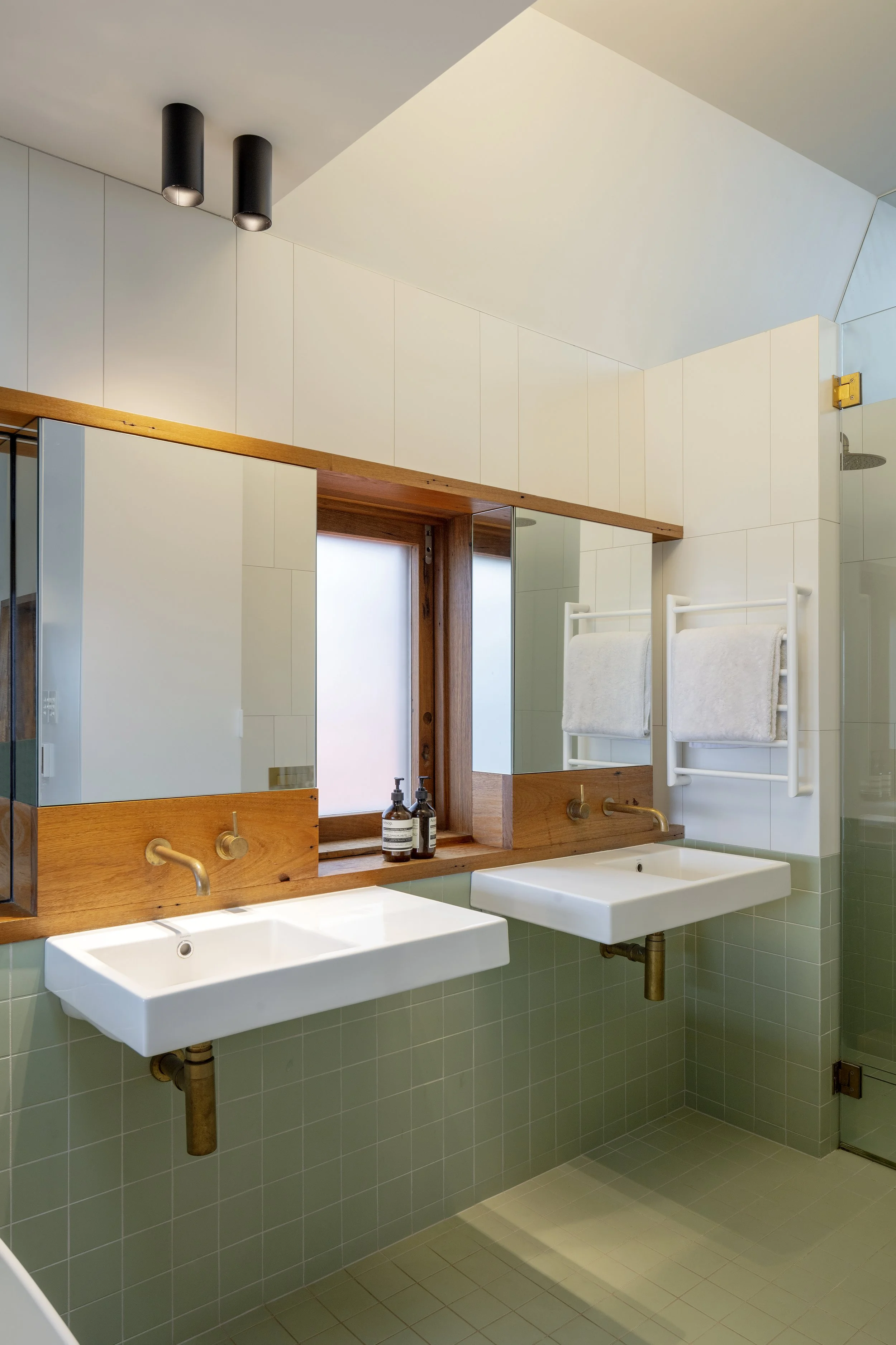 Bathroom with twin wall-hung basins, timber-framed mirrors and sage-green tiles.