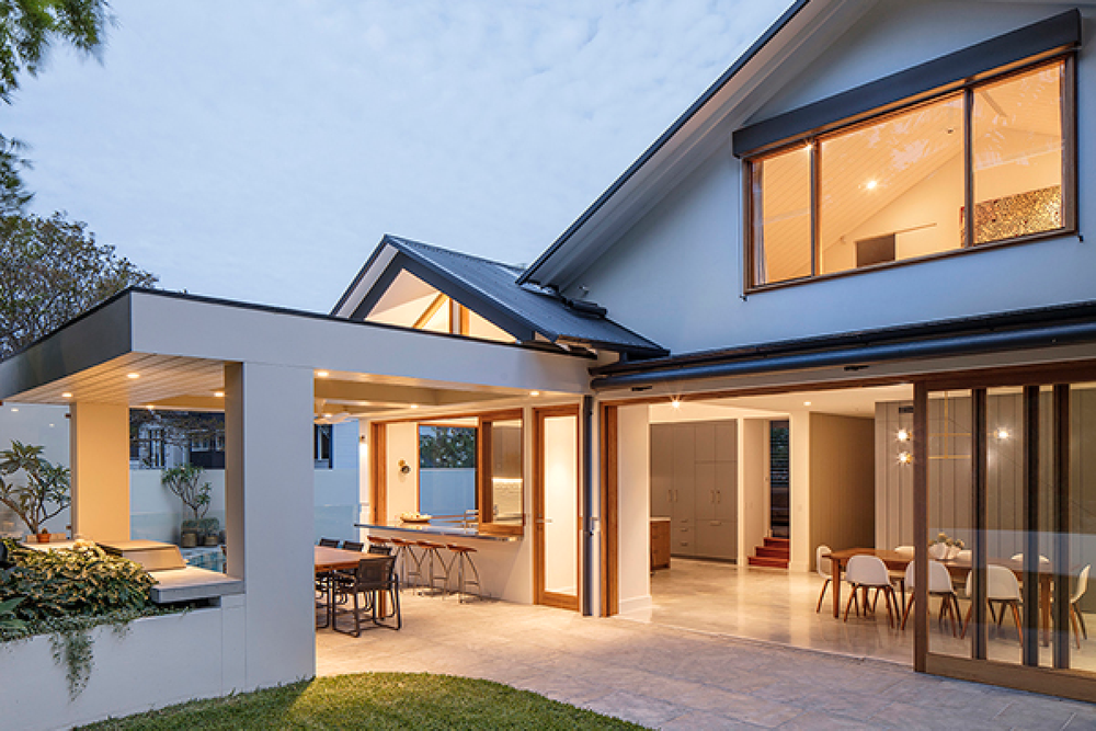 Modern house with open living and dining areas, large windows, and a patio, illuminated at dusk.