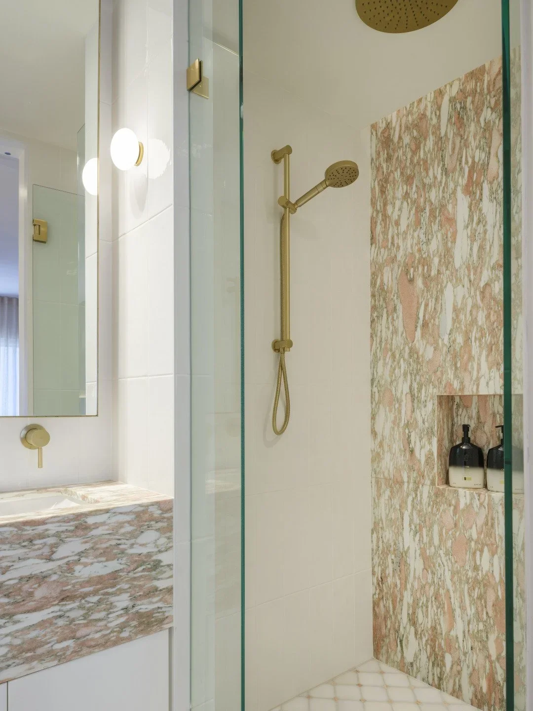 Modern bathroom shower area with a gold showerhead, a tiled accent wall, and a built-in shelf with toiletries.