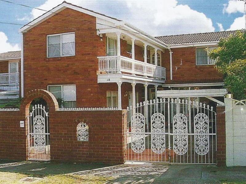 A two-story brick house with a white balcony and decorative white metal gate and fence.