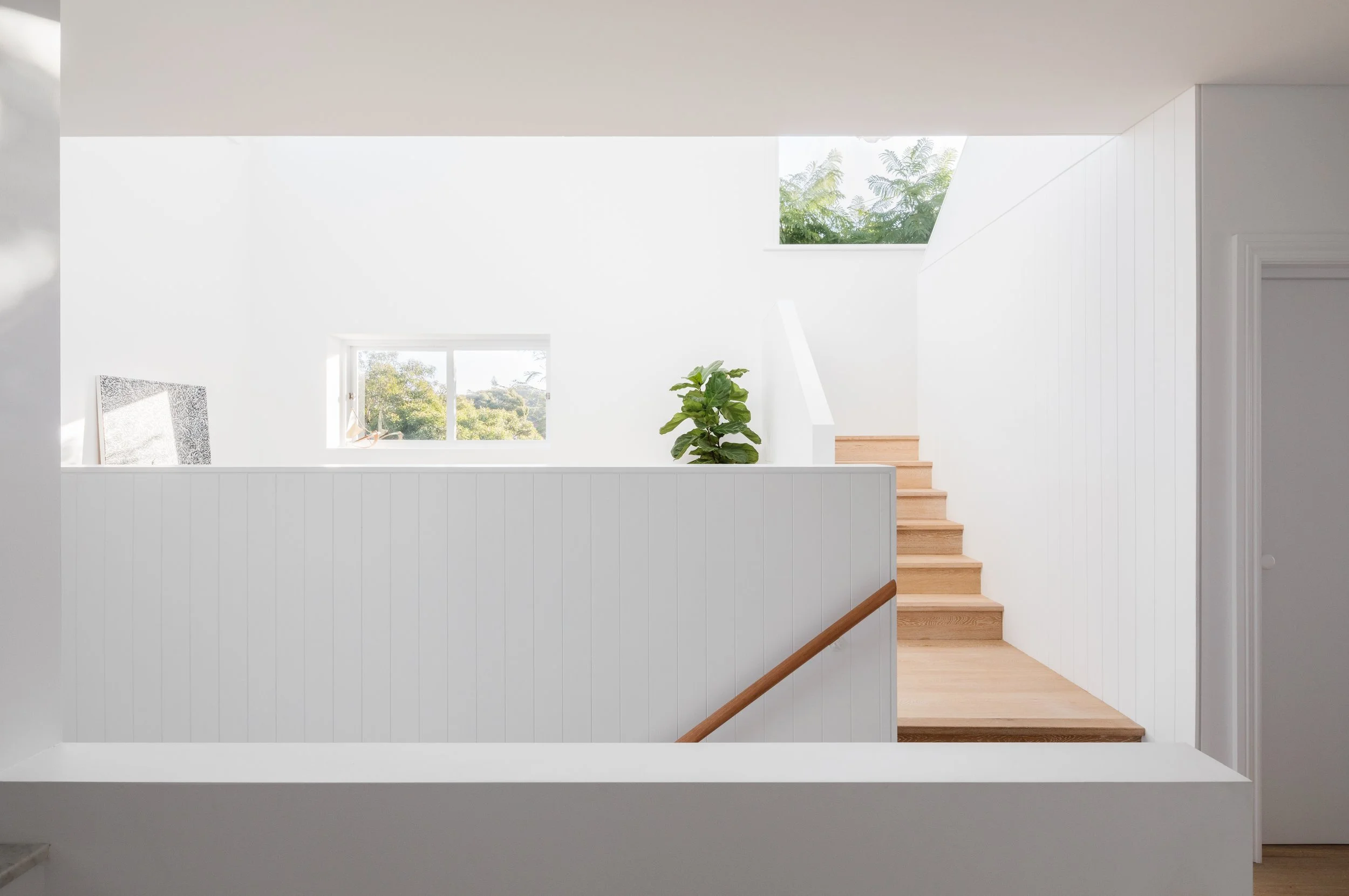 Light-filled stair landing with timber steps, white-lined walls and skylight bringing natural light into the interior.