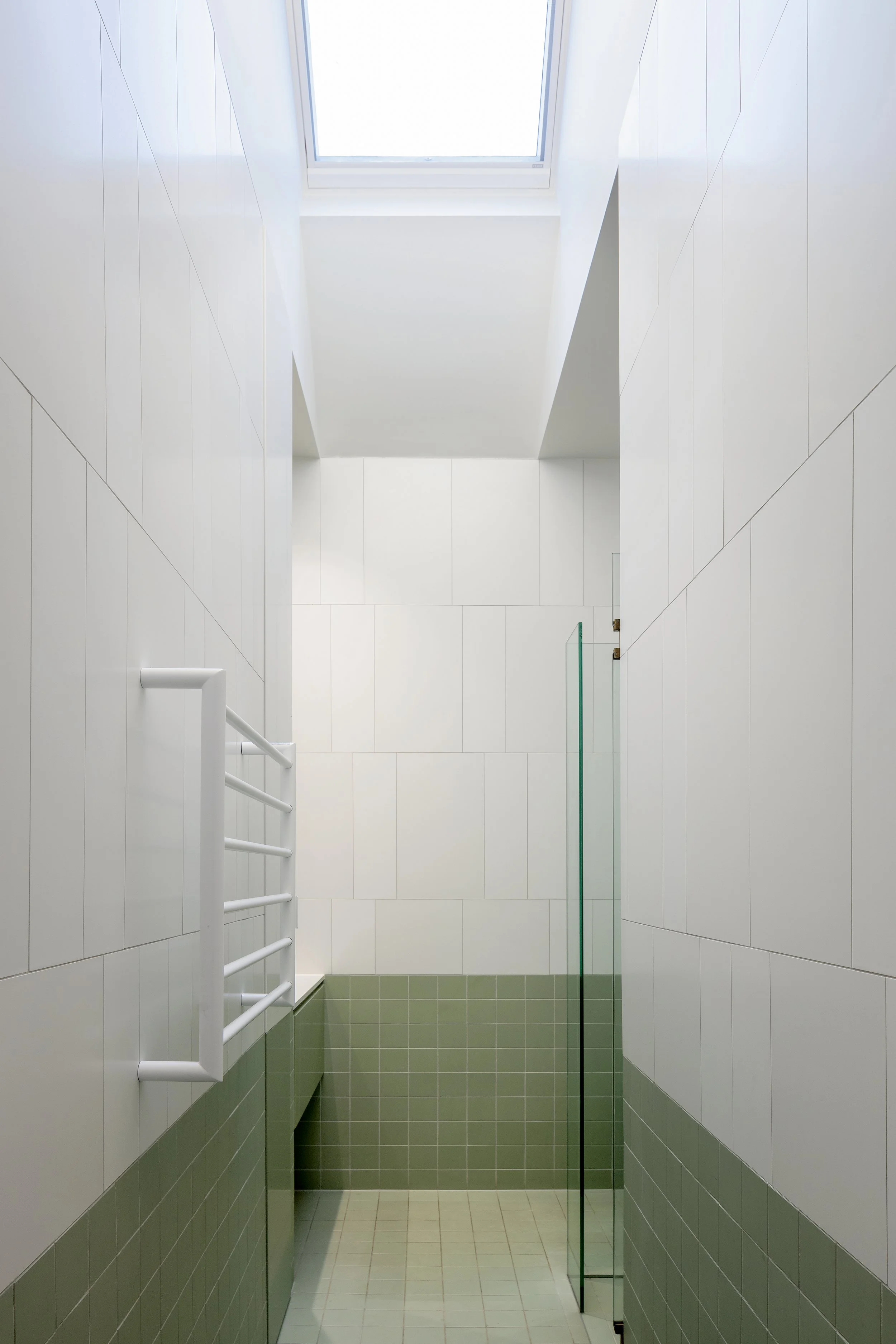 Narrow bathroom with white tiled walls, sage-green lower tiles and an overhead skylight.