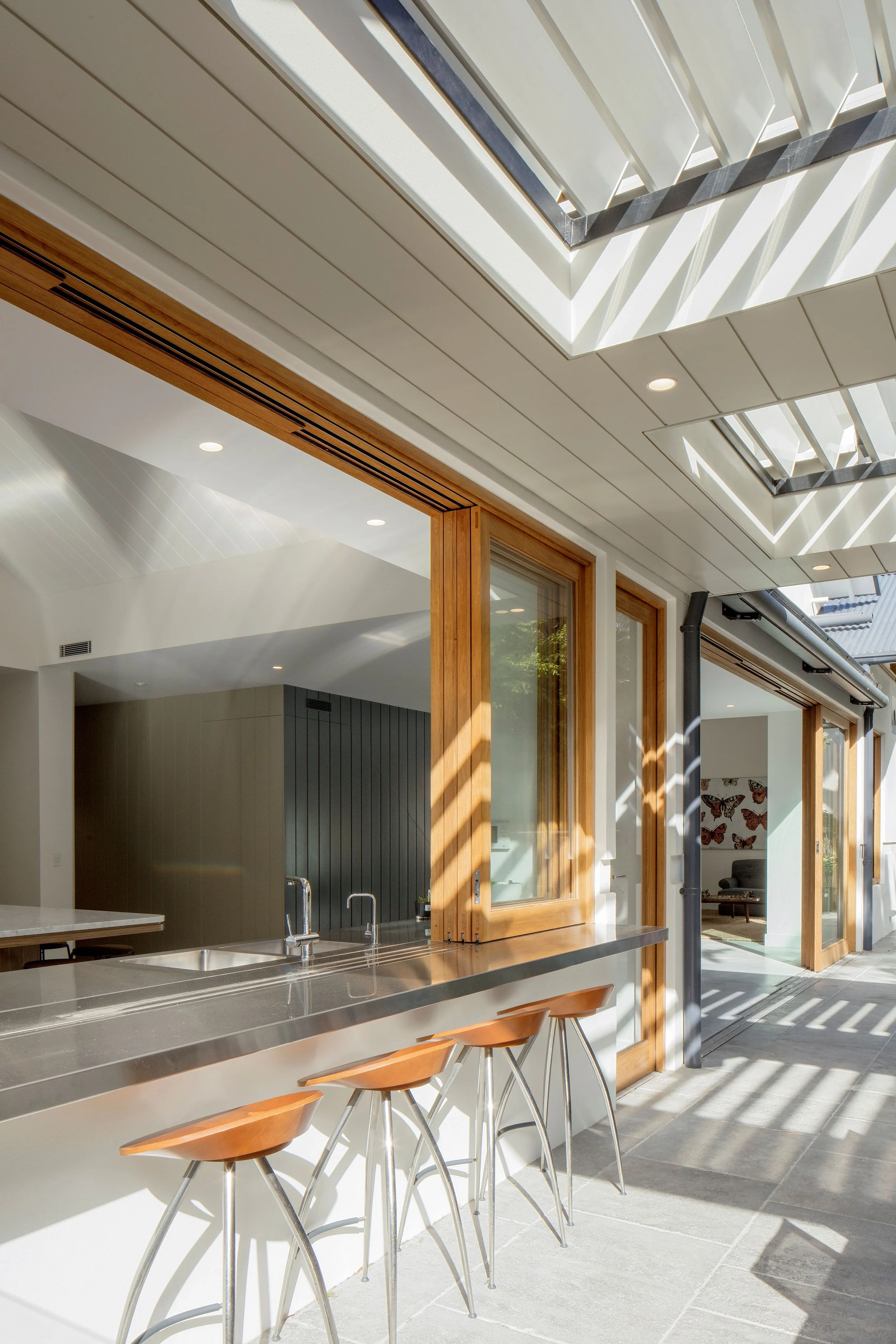 Light-filled indoor-outdoor kitchen at Bronte House, featuring timber bifold windows, a stainless-steel bench and overhead skylights.