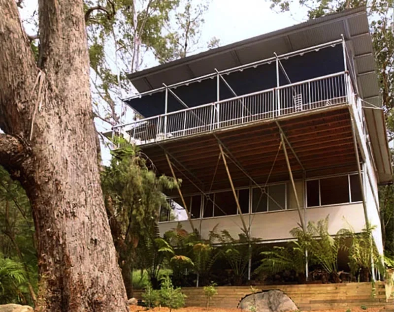 A multi-story house built on stilts among trees in a forested area.