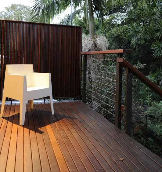 A wooden balcony with a white chair, surrounded by lush green trees and plants.