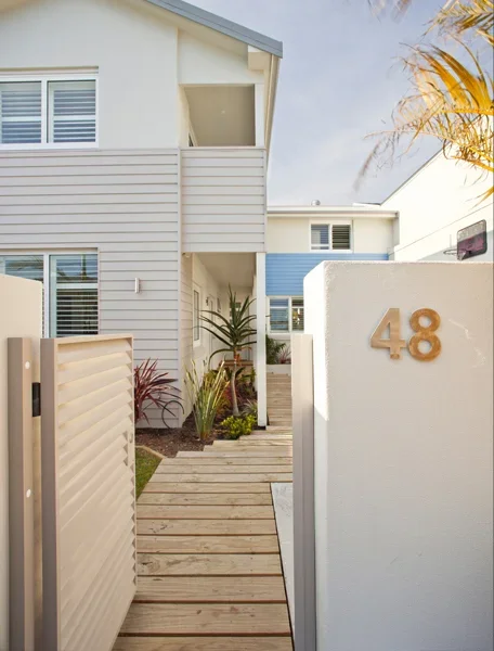 Modern house with white walls, large windows, and a wooden pathway entrance, marked with the number 48 on a white wall
