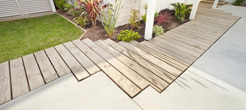 Wooden deck next to a garden with various plants and a concrete walkway.