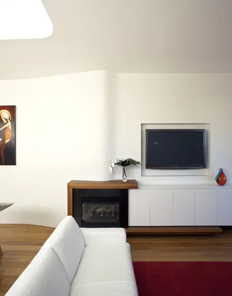 Living room with a white couch, a TV mounted on the wall, a fireplace with a flower vase on top, and a colorful vase on the shelf below the TV.