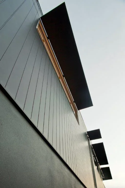 View of an outdoor building facade with large black screens and metal siding, taken from below.