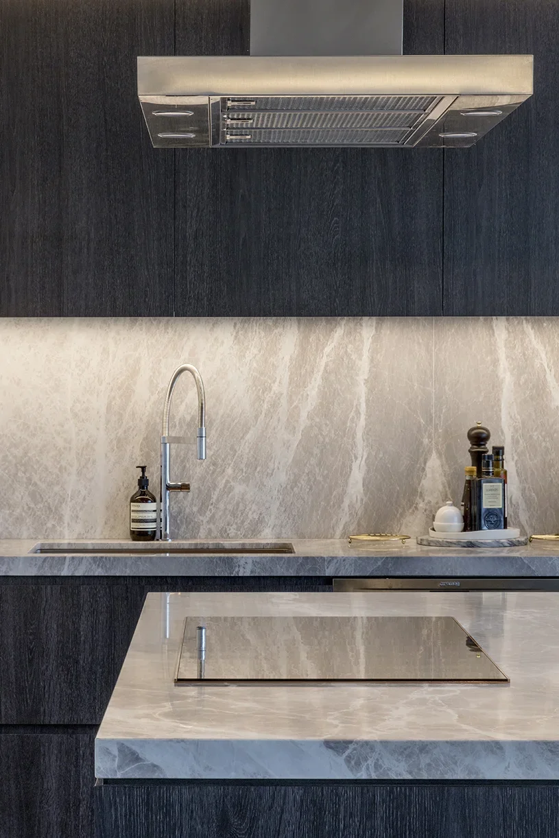 Modern kitchen with marble countertops, a sink with a brushed metal faucet, black cabinets, and a built-in stovetop.