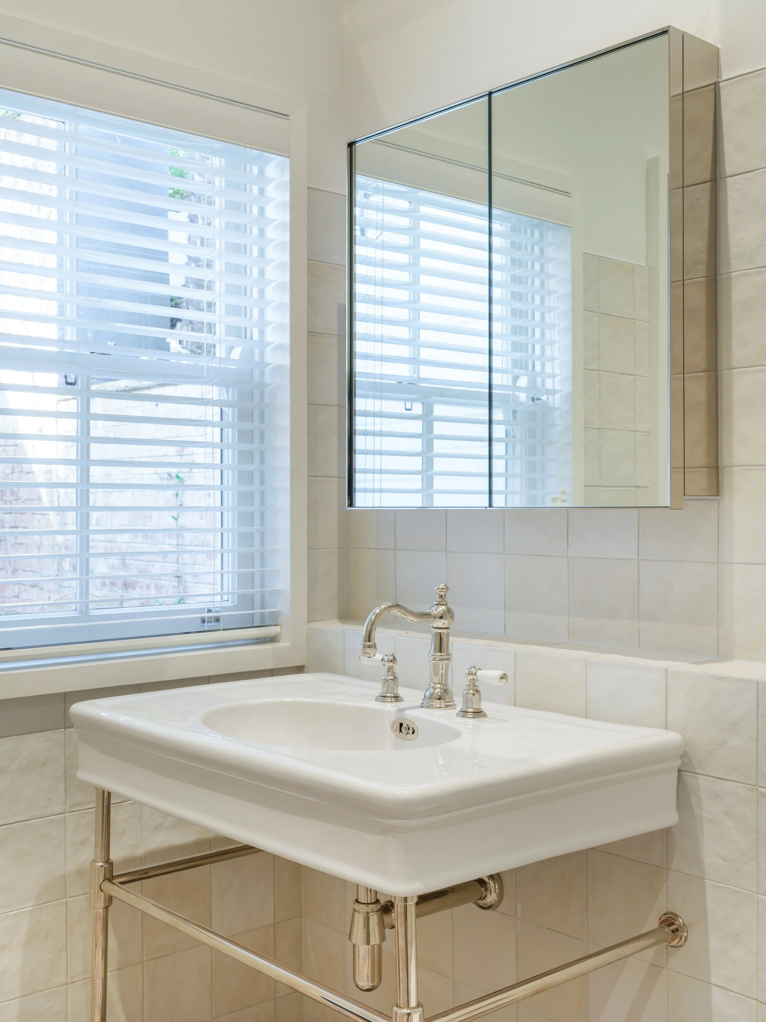Light-filled bathroom at Vaucluse house with white tiles, a traditional basin, chrome tapware and a mirrored cabinet.