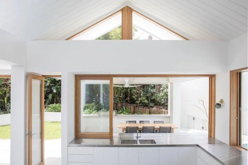 Modern kitchen with white cabinets, large windows, and view of outdoor garden.