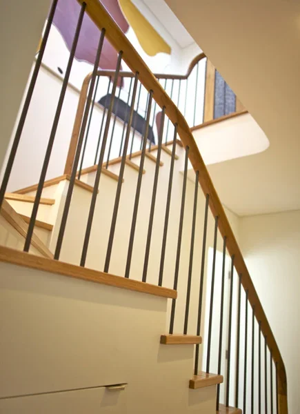 Interior view of a wooden staircase with black metal railings, leading to the upper floor of a house.