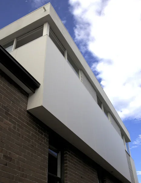 Modern white apartment building balcony with glass railing, set against a partly cloudy sky.
