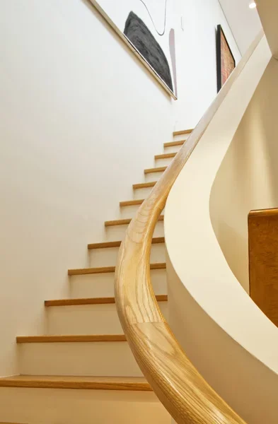 Interior view of a staircase with wooden steps and a curved wooden handrail, decorated with abstract paintings on the wall.