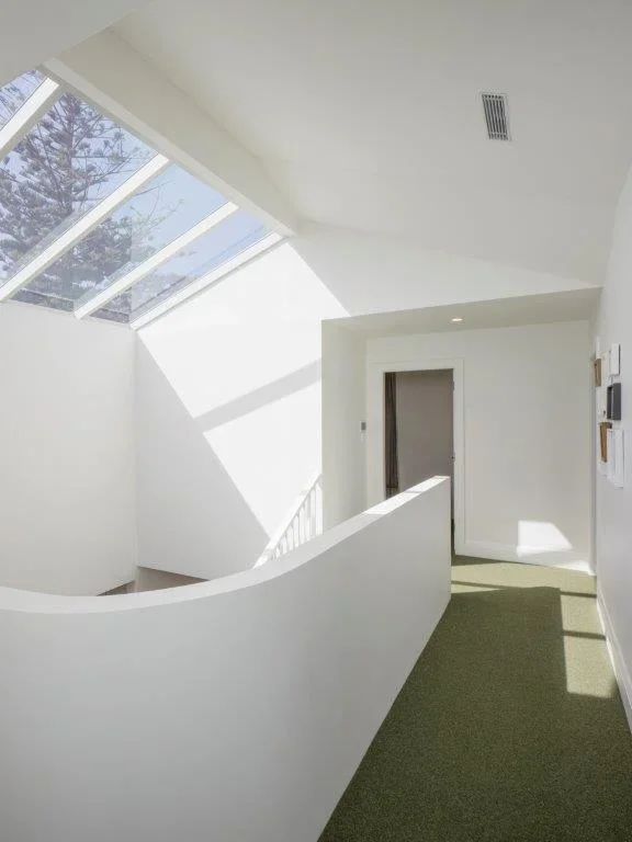 Bright modern interior with a large skylight, white walls, and a green carpet, leading to an open doorway.