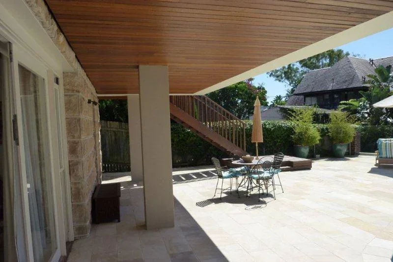 A backyard patio with a table and chairs, large potted plants, an umbrella, and a staircase leading to an upper level.