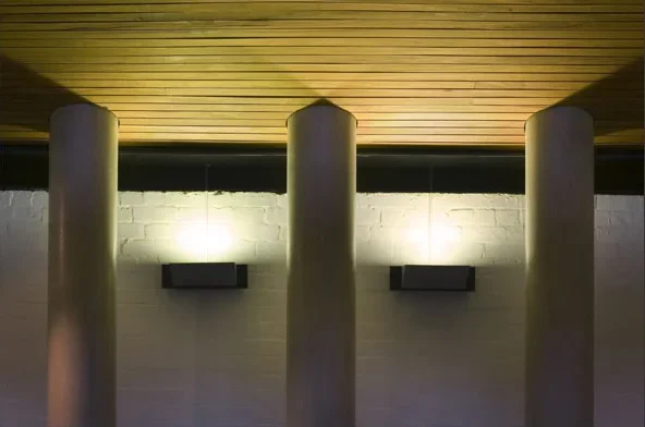 Photo of three large white columns on a wall with a wooden ceiling and modern wall-mounted lights.