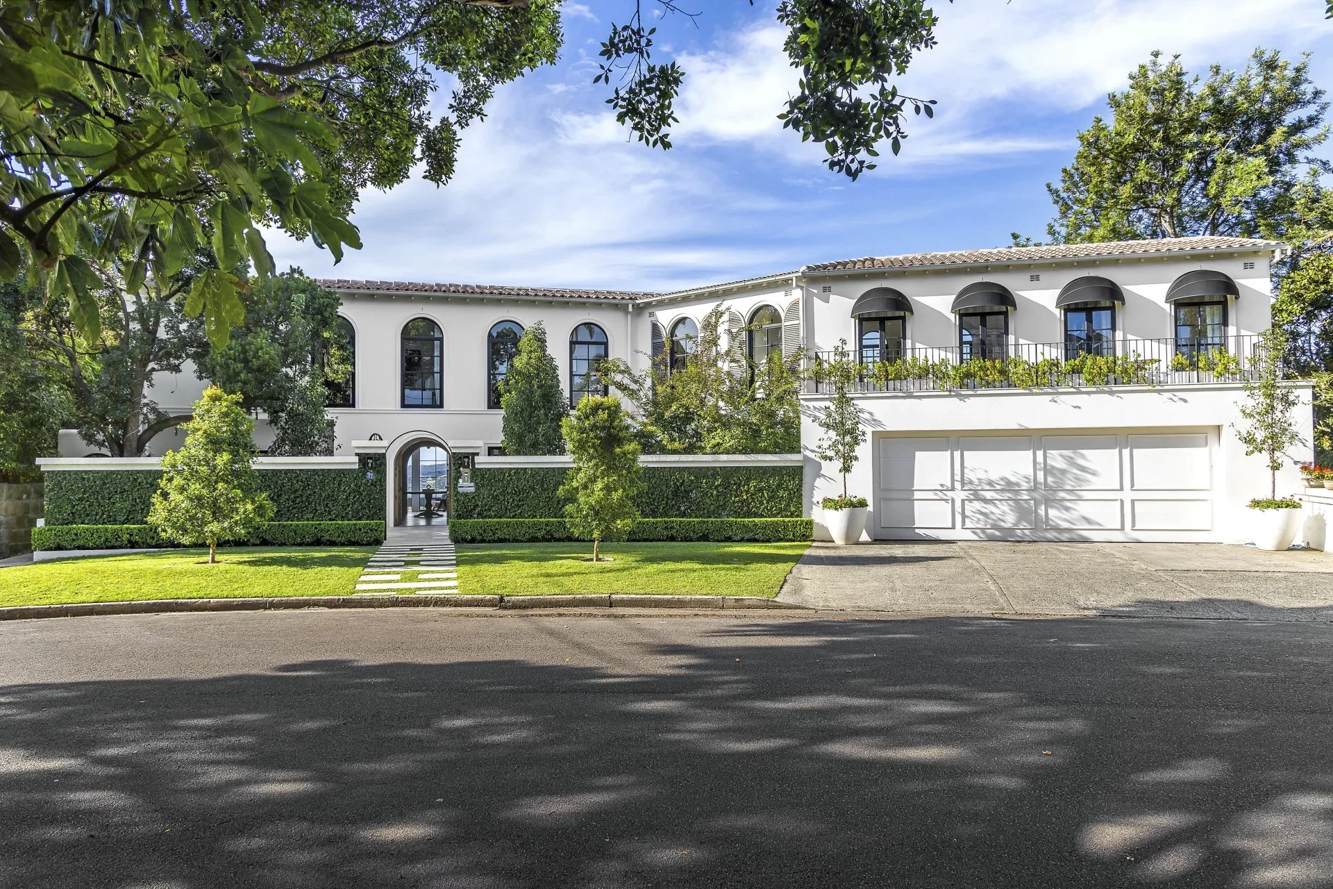 Front view of a modern white two-story house with black awnings, large arched windows, a garage, and a well-maintained lawn with trees.