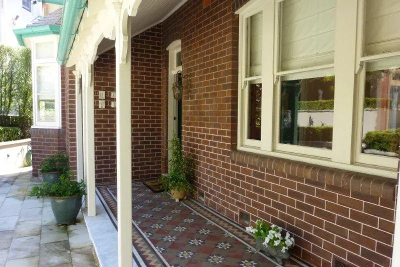 Front porch of a brick house with potted plants, a patterned tile floor, and a wreath on the door.