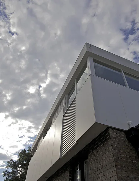 Close-up of a modern building corner with white panels and large windows under cloudy sky.