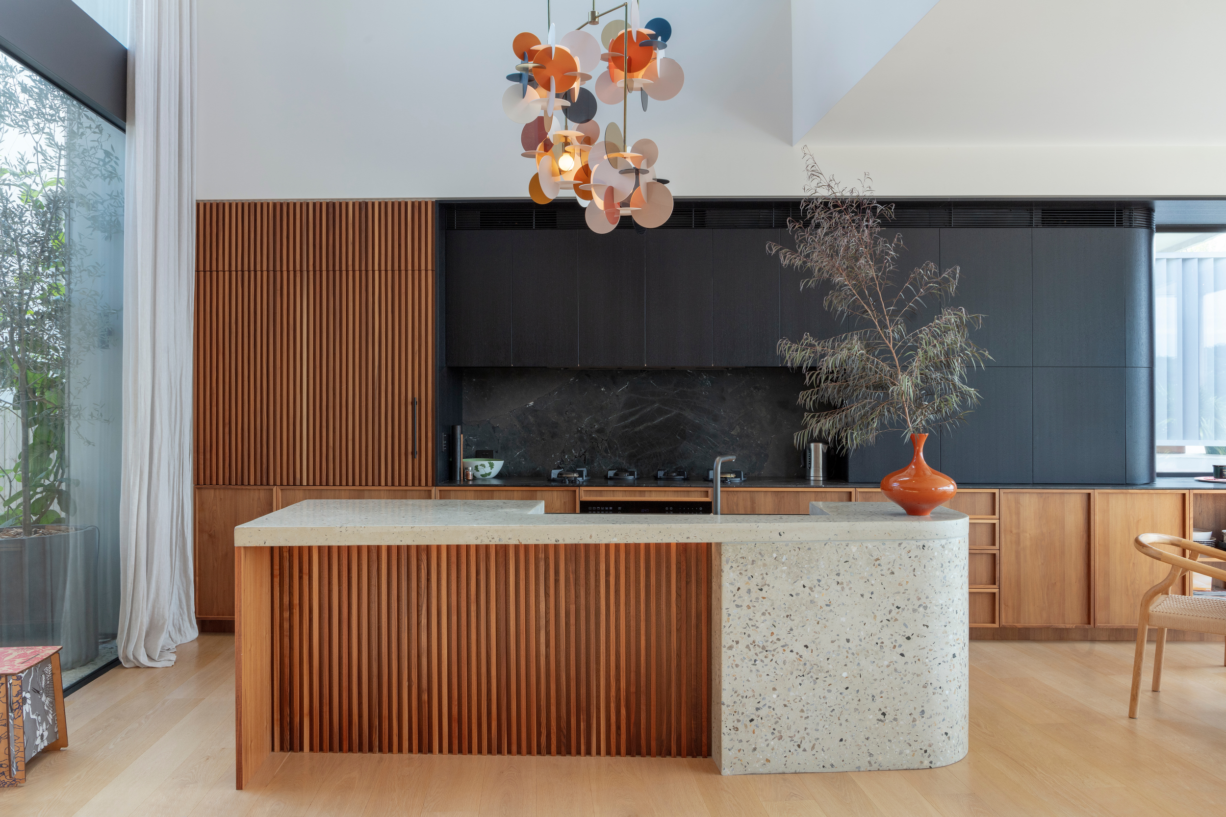 A striking kitchen in the Bronte House project by To The Mil, featuring a terrazzo island, vertical timber battens and bold statement lighting that adds warmth and character to the open living space.