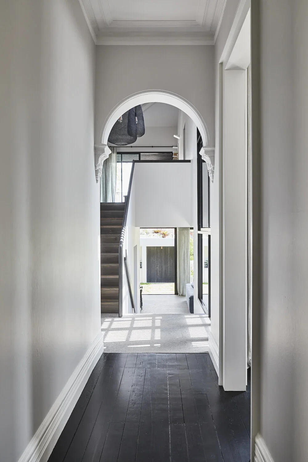 View through a hallway into a modern living space with stairs and large window with curtains.