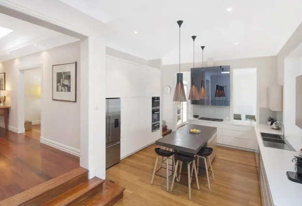 Modern kitchen with white cabinets, stainless steel appliances, black pendant lights, dark wood island with four chairs, and hardwood floors.
