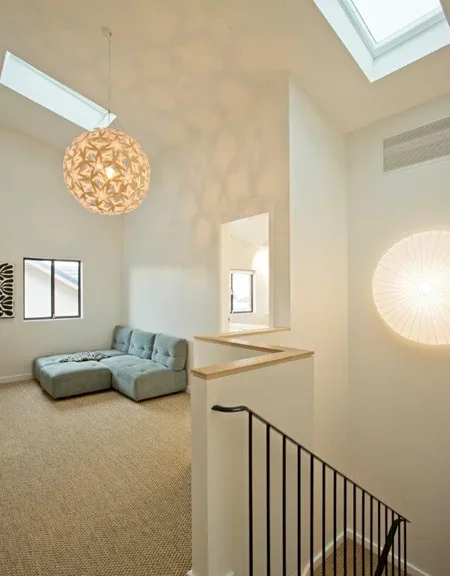 Living room with high ceiling, skylights, a beige sectional sofa, framed artwork, and a decorative wall feature