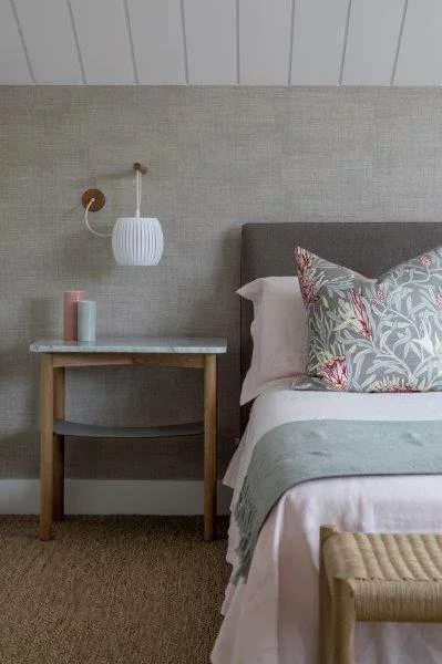 Close-up of a neatly made bed with decorative pillows, a small wooden side table with candles, and a modern wall-mounted lamp in a contemporary bedroom.