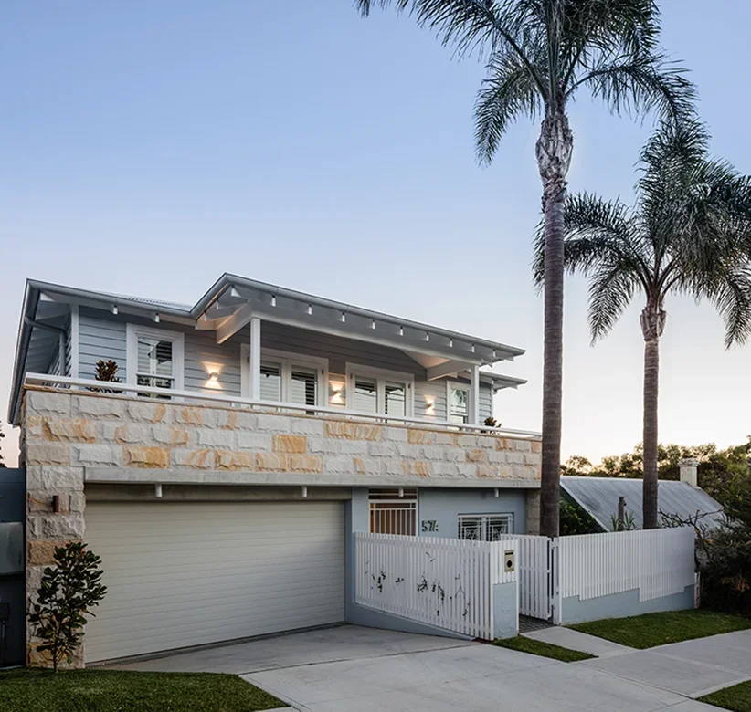 Modern two-story house with white and beige exterior, palm trees in front, and a driveway with a garage door.