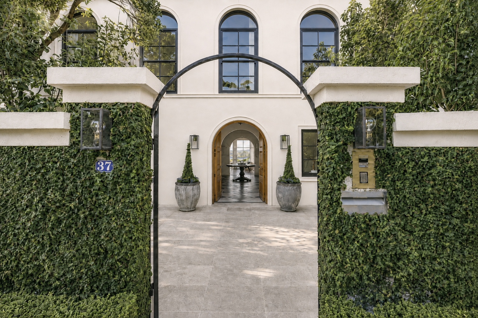 Entrance to a modern white house with black window frames, a black arched gate, and plants in large concrete pots.