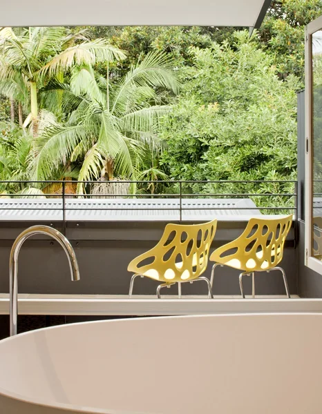 A balcony with two yellow modern chairs overlooking lush green tropical trees.