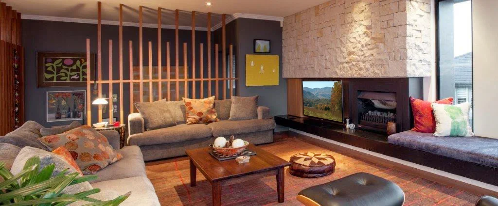 Cozy living room with two gray sofas, wooden coffee table, fireplace, and window seat with cushions, decorated with wall art and a plant.