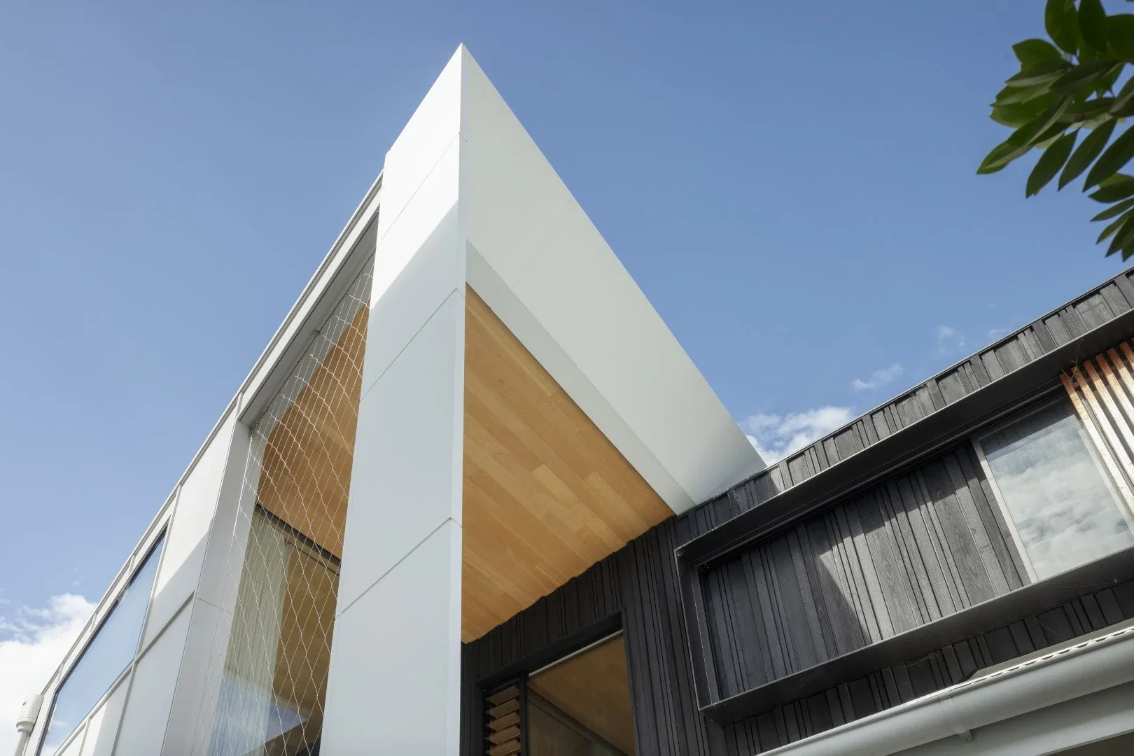 Low-angle view of a modern building with white, black, and wooden exterior panels under a blue sky with some clouds.
