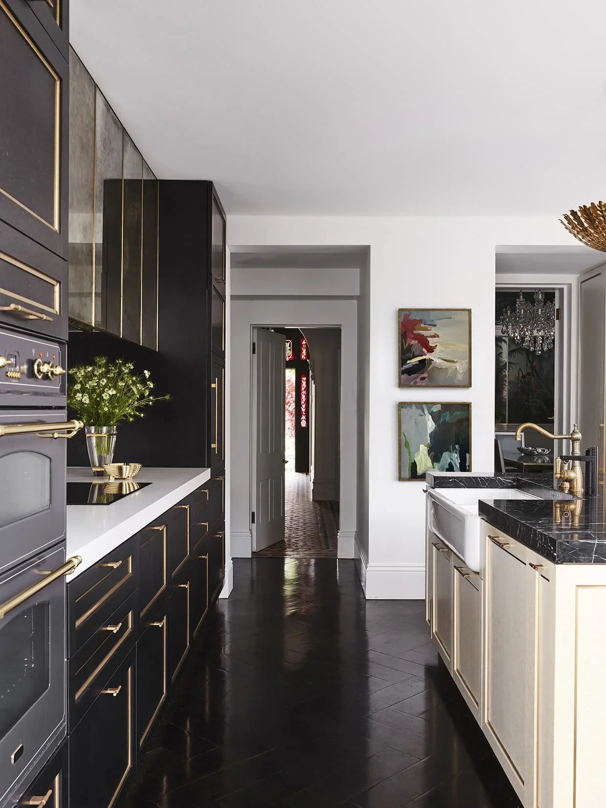 Modern kitchen with black and white cabinetry, gold accents, black marble countertop, farmhouse sink, and abstract artwork on the wall.