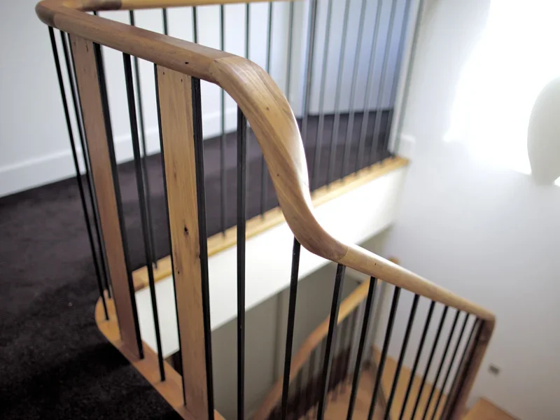 A staircase railing with a wooden handrail and black metal balusters, viewed from the top looking down.