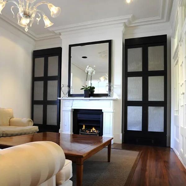Living room with a fireplace, black cabinets, a mirror above the fireplace, a wooden coffee table, beige upholstered furniture, and a white orchid on the mantel.