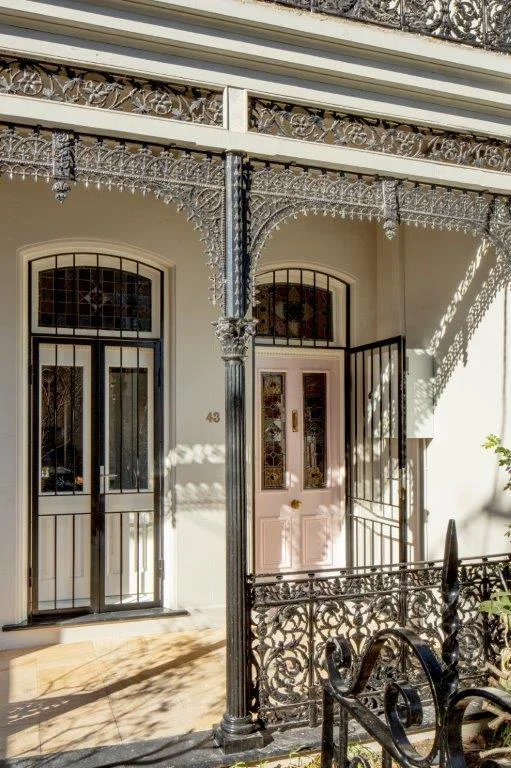 Victorian-style front porch with decorative ironwork, two doors with stained glass panels, and cast iron railing in black.