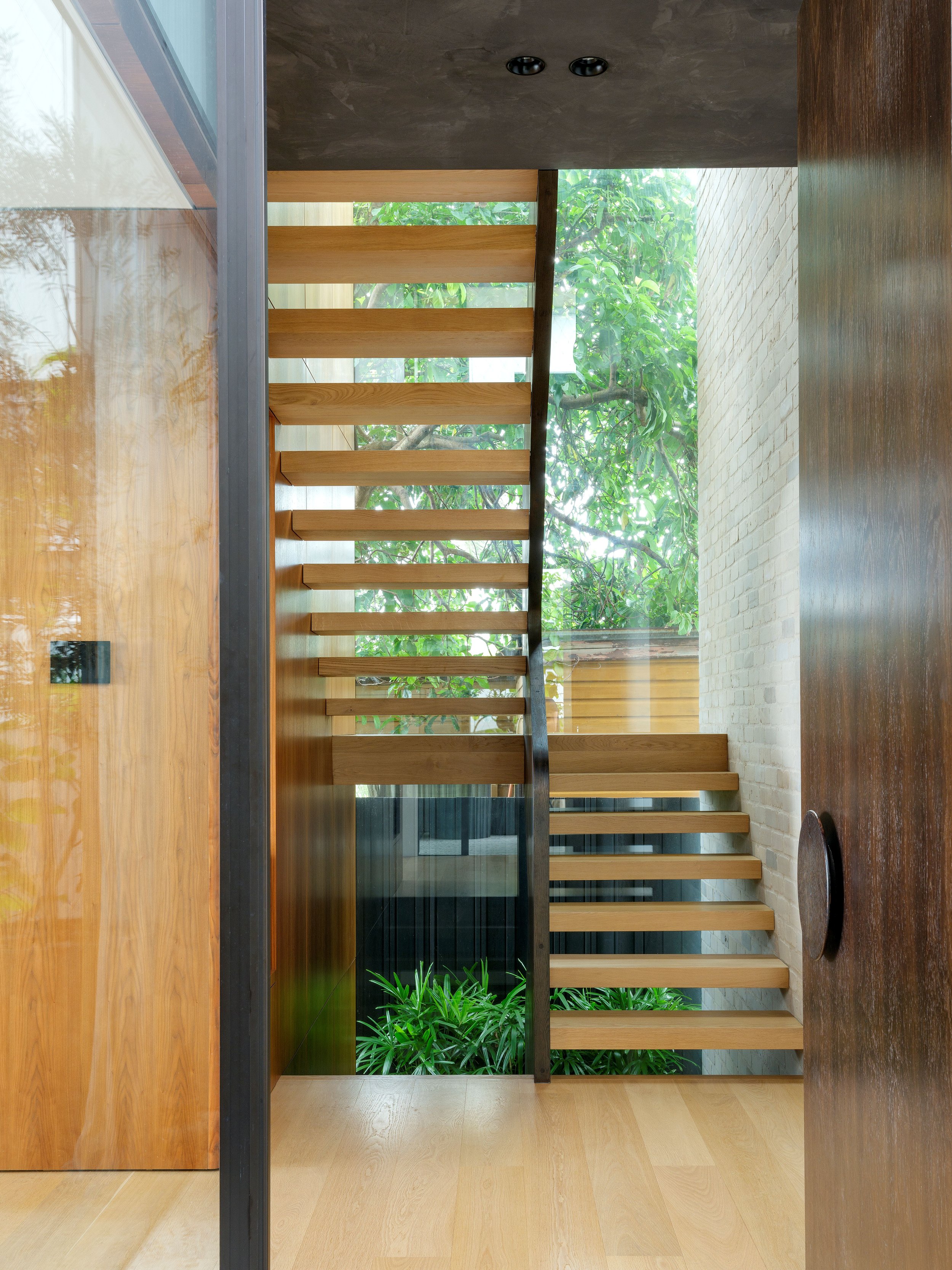 View through a doorway to open timber stairs and a steel balustrade overlooking a planted courtyard.