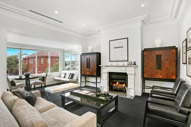 Living room with a fireplace, black coffee table, beige sofa, black armchairs, large windows, and modern decor.