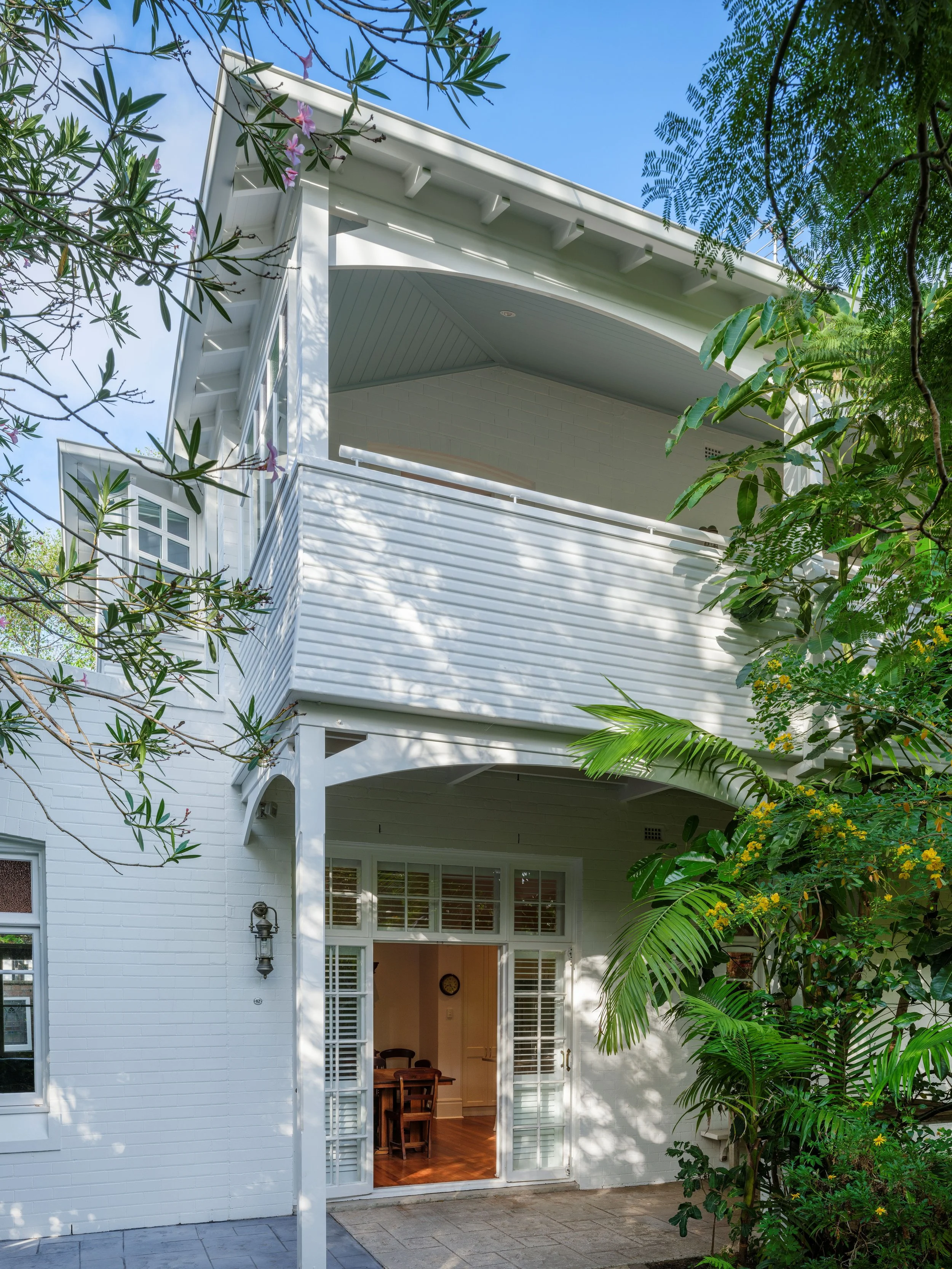 Rear exterior Vaucluse home, featuring a white weatherboard façade, covered balconies and a lush established garden.