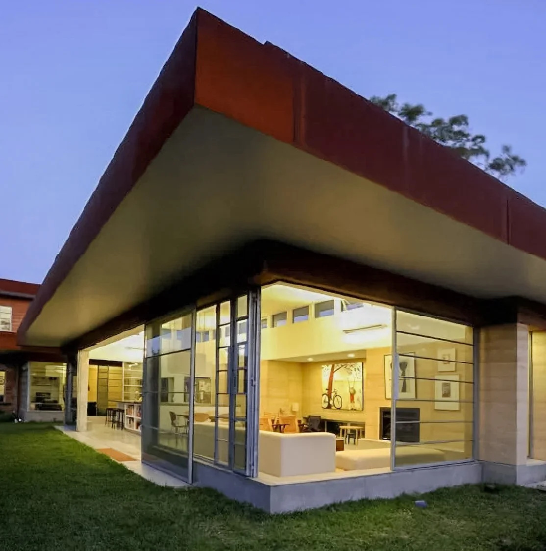 Modern house with large glass windows, a sloped roof, and interior lighting visible from outside during dusk.