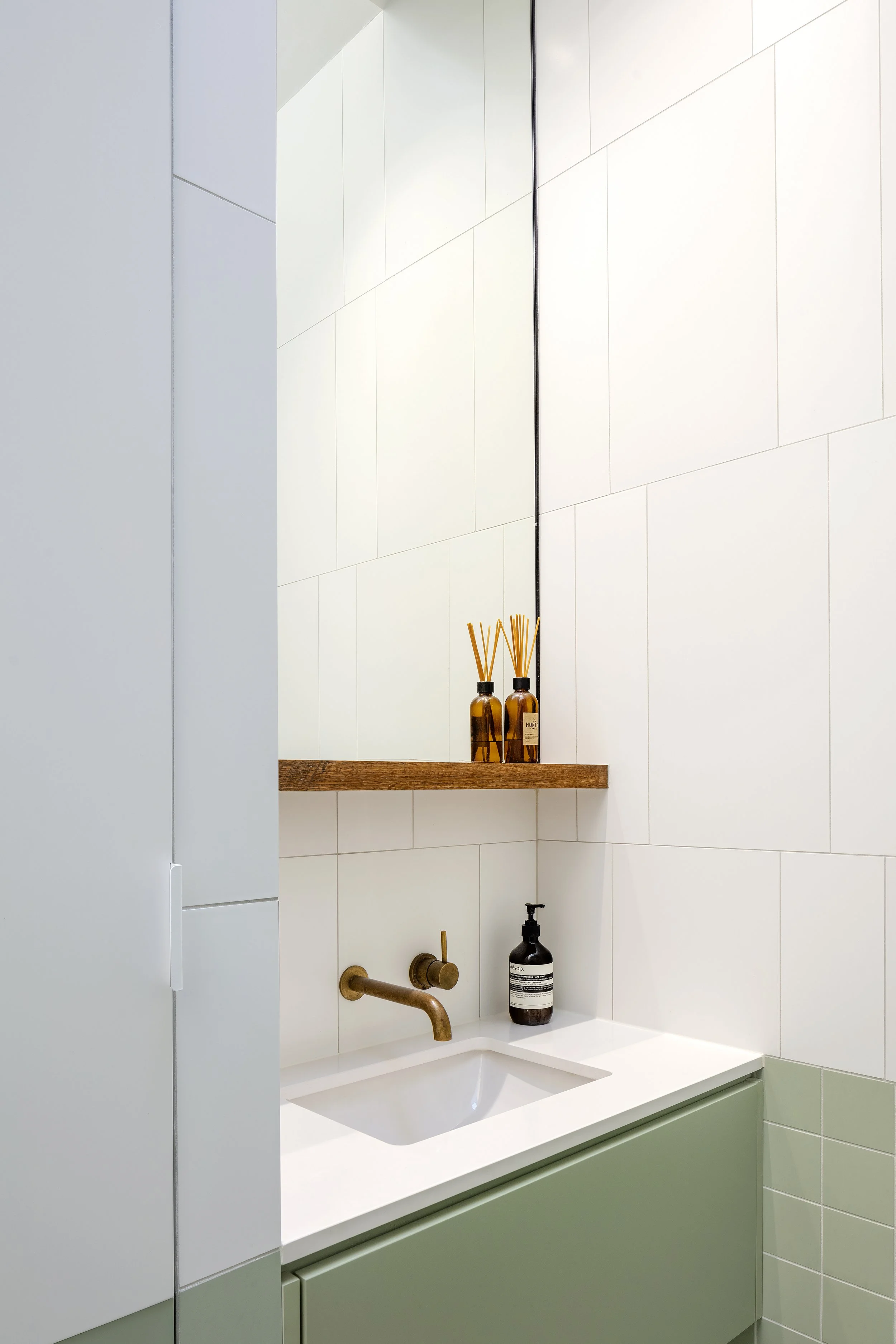 Compact bathroom vanity with a white basin, sage-green tiles and brass tapware.