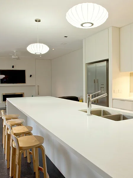 Modern kitchen with a white countertop island, wooden barstools, and pendant lighting fixtures.